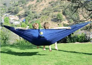 two campers in blue hammock overlooking forest