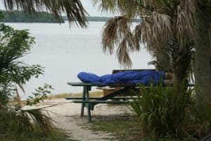 man sleeping on picnic table with blue sleeping bag