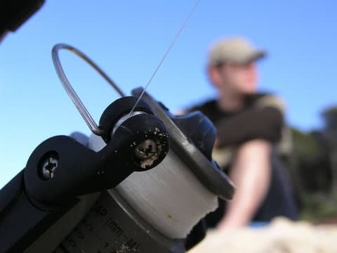 Close up fishing reel angler in background